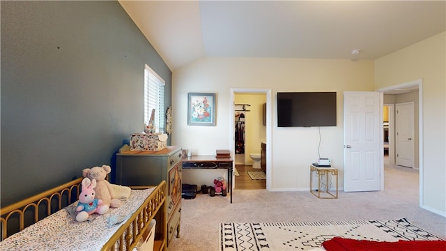 carpeted bedroom with a walk in closet, ensuite bathroom, and vaulted ceiling