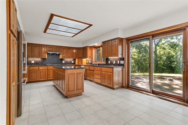 kitchen with light tile patterned flooring, backsplash, stainless steel refrigerator, and a kitchen island