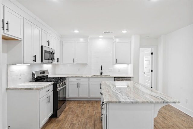 4206 SW Adams St, Bentonville, AR 72713 - kitchen with stainless steel appliances, a sink, light wood-style floors, a kitchen island, and white cabinets