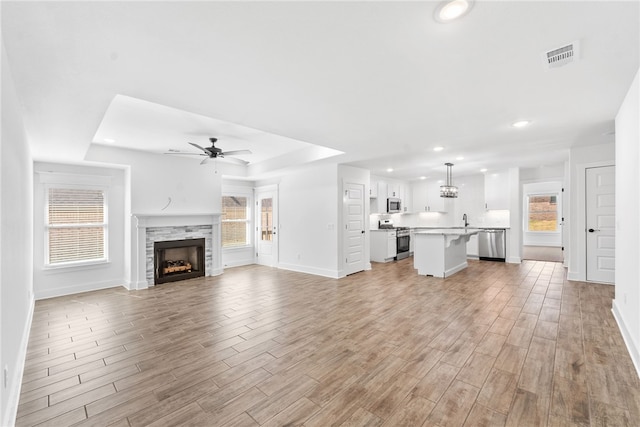 unfurnished living room featuring ceiling fan, a raised ceiling, sink, and light hardwood / wood-style flooring