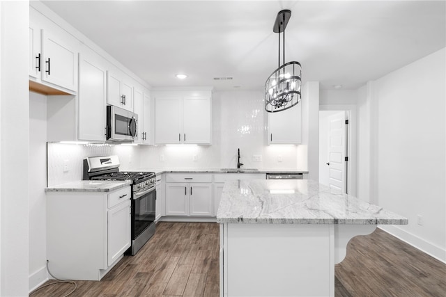 kitchen with pendant lighting, white cabinetry, sink, stainless steel appliances, and light stone countertops