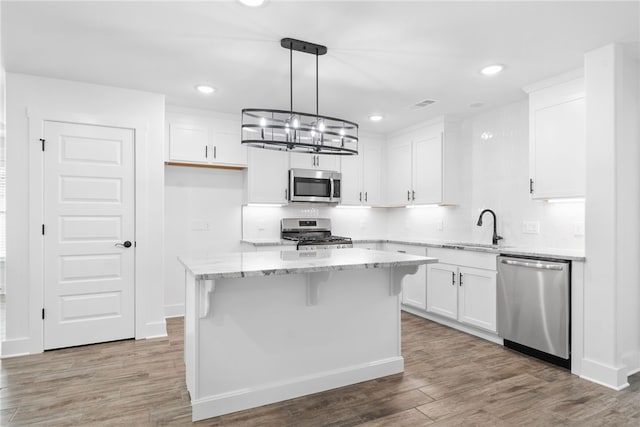 kitchen with a kitchen island, white cabinetry, sink, hanging light fixtures, and stainless steel appliances