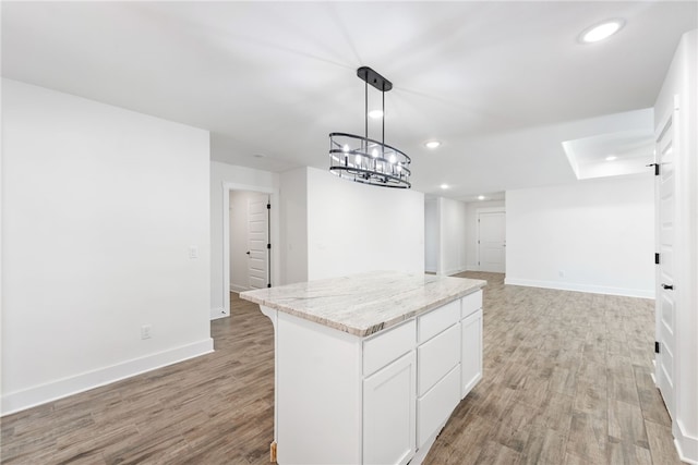 kitchen with light stone counters, light hardwood / wood-style floors, white cabinets, a kitchen island, and decorative light fixtures