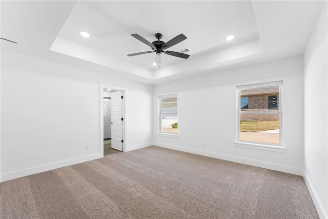 carpeted empty room with ceiling fan and a tray ceiling