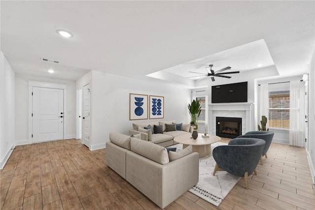 living room with light hardwood / wood-style floors, a raised ceiling, and ceiling fan