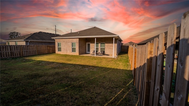 back house at dusk with a patio and a lawn