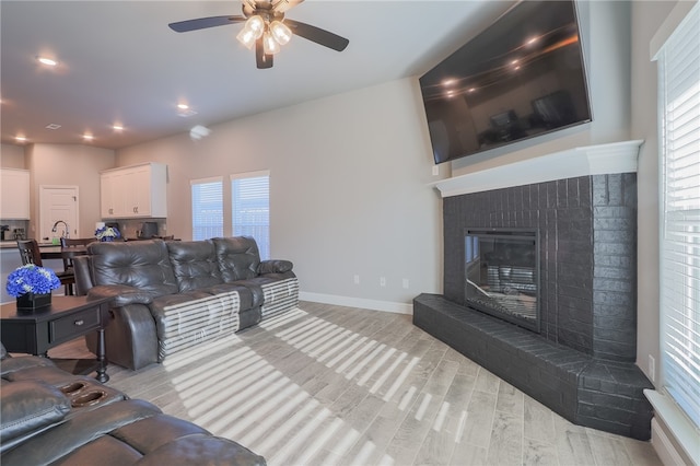 living room with a fireplace, light wood-type flooring, and ceiling fan