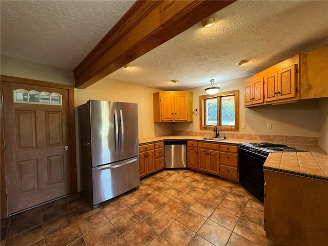 kitchen featuring stainless steel appliances, sink, tile counters, beam ceiling, and a textured ceiling