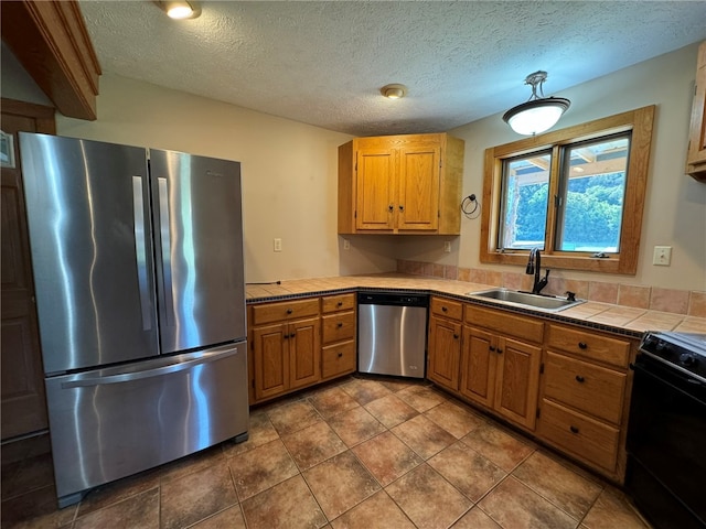 kitchen with sink, a textured ceiling, appliances with stainless steel finishes, tile counters, and tile patterned flooring