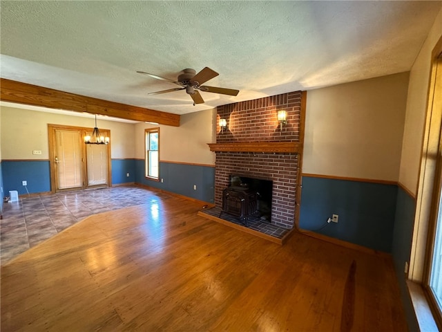 unfurnished living room featuring wood-type flooring, a textured ceiling, a wood stove, and ceiling fan