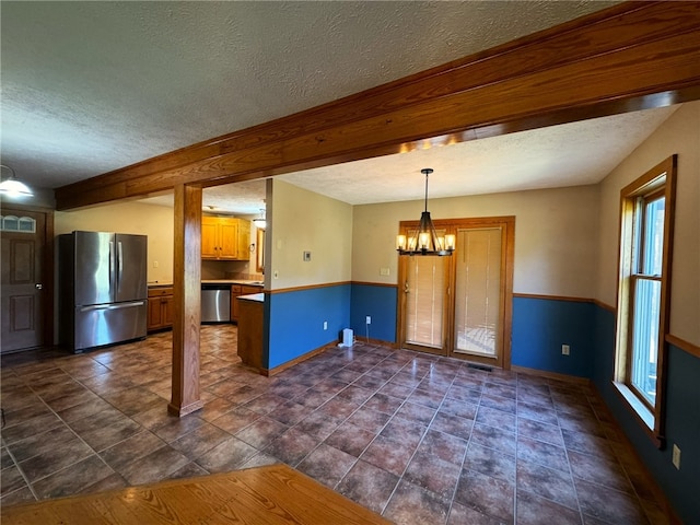 kitchen with beamed ceiling, a notable chandelier, appliances with stainless steel finishes, decorative light fixtures, and a textured ceiling