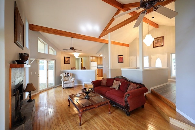 living room featuring hardwood / wood-style floors, beam ceiling, a tiled fireplace, ceiling fan, and high vaulted ceiling