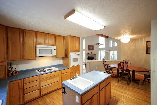 kitchen with a center island with sink, ceiling fan, light hardwood / wood-style flooring, sink, and white appliances