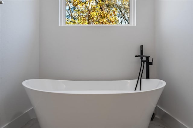 bathroom featuring a freestanding bath, marble finish floor, and baseboards