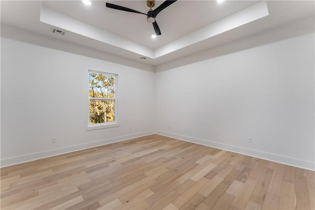 spare room with light wood-style floors, baseboards, a raised ceiling, and a ceiling fan