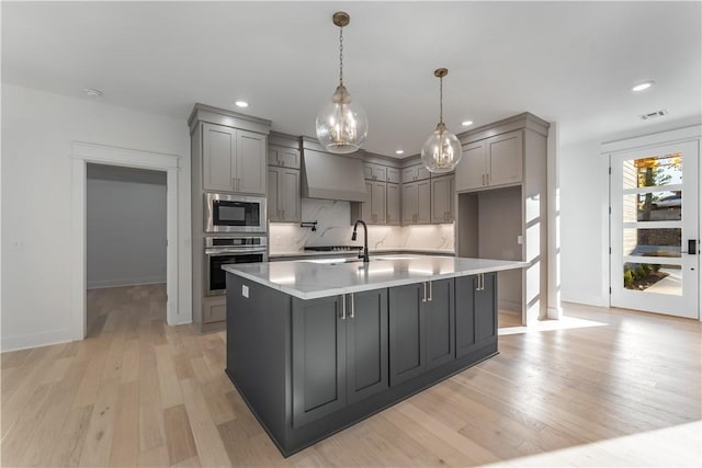 kitchen with gray cabinets, light wood-type flooring, stainless steel appliances, and an island with sink