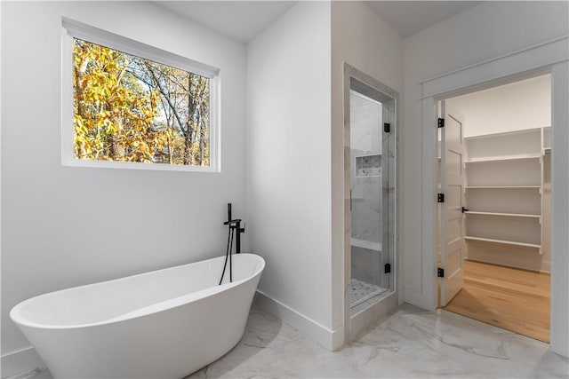 full bathroom featuring baseboards, a freestanding bath, marble finish floor, a stall shower, and a walk in closet