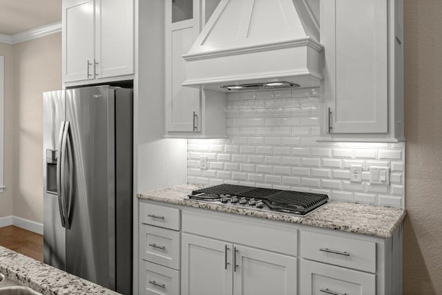 kitchen with light stone counters, white cabinets, custom exhaust hood, stainless steel appliances, and decorative backsplash