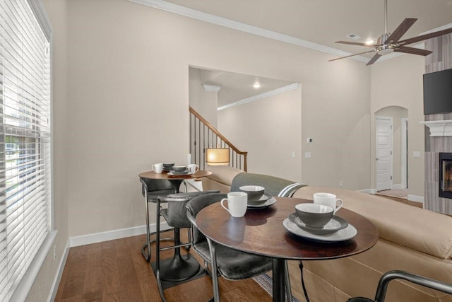 dining space with ceiling fan, ornamental molding, dark hardwood / wood-style flooring, and a tile fireplace