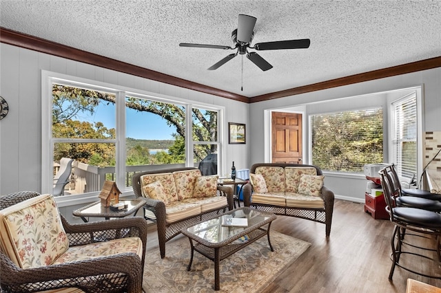 living room with wood-type flooring, a textured ceiling, crown molding, and a healthy amount of sunlight