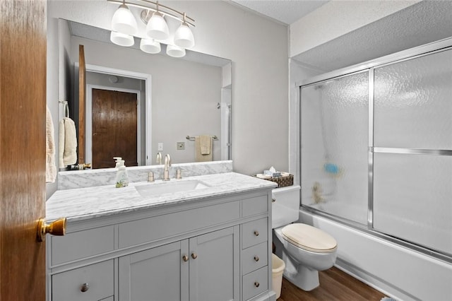 full bathroom with vanity, shower / bath combination with glass door, toilet, a textured ceiling, and wood-type flooring