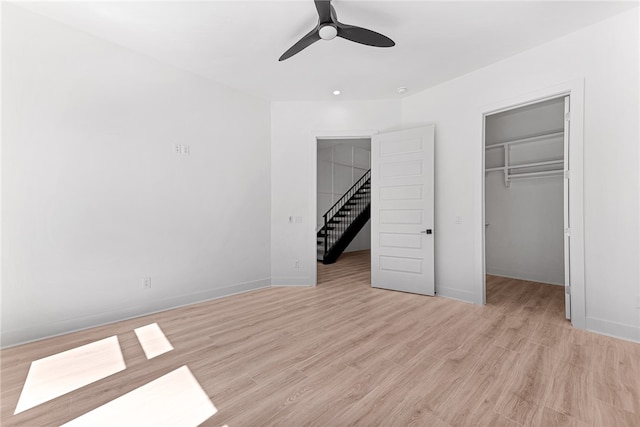 unfurnished bedroom with a walk in closet, light wood-type flooring, and ceiling fan