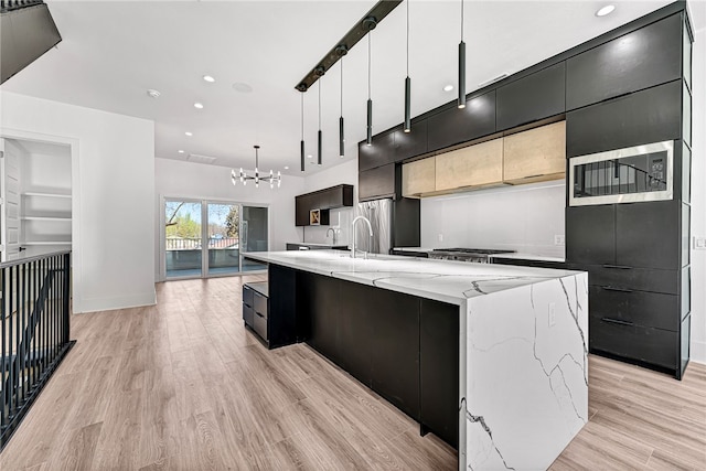 kitchen with light wood-type flooring, hanging light fixtures, a chandelier, a spacious island, and appliances with stainless steel finishes