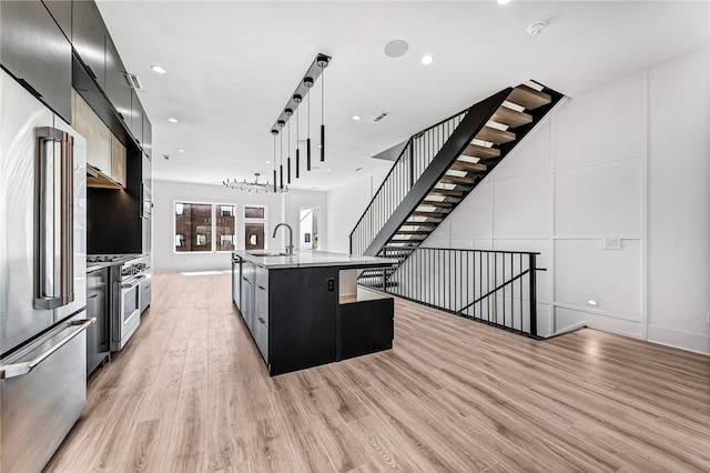 kitchen featuring light hardwood / wood-style floors, pendant lighting, high quality appliances, sink, and an island with sink