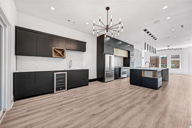 kitchen featuring pendant lighting, beverage cooler, a kitchen island with sink, appliances with stainless steel finishes, and light wood-type flooring