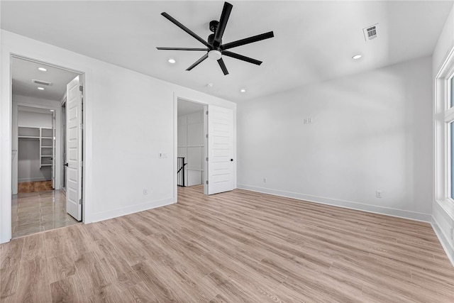 unfurnished bedroom featuring a spacious closet, light hardwood / wood-style floors, a closet, and ceiling fan