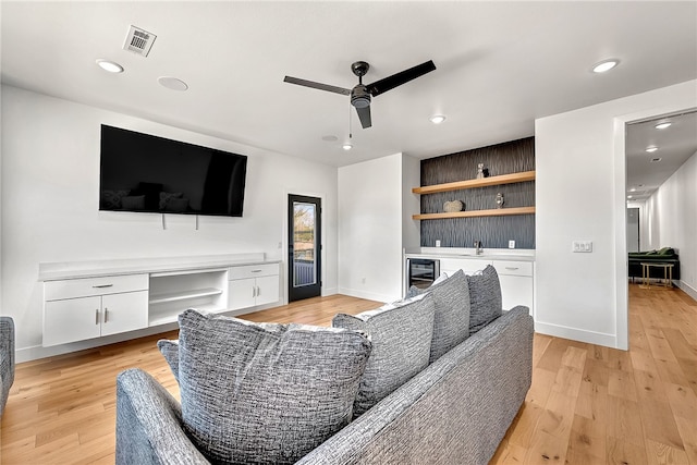 living room featuring ceiling fan, beverage cooler, light hardwood / wood-style flooring, and built in desk