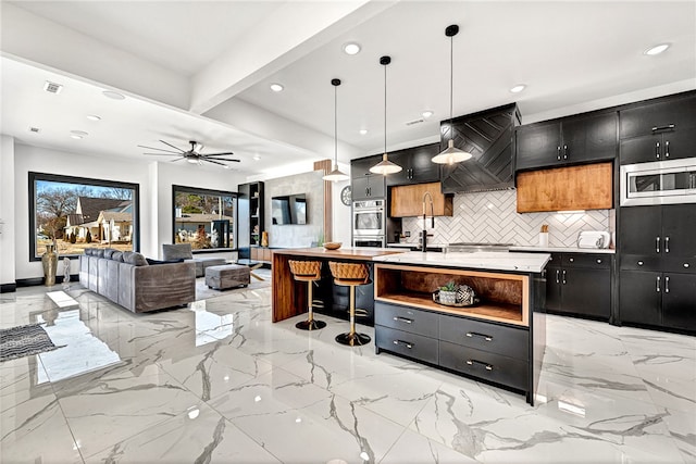 kitchen featuring beamed ceiling, decorative light fixtures, a center island with sink, stainless steel appliances, and custom exhaust hood