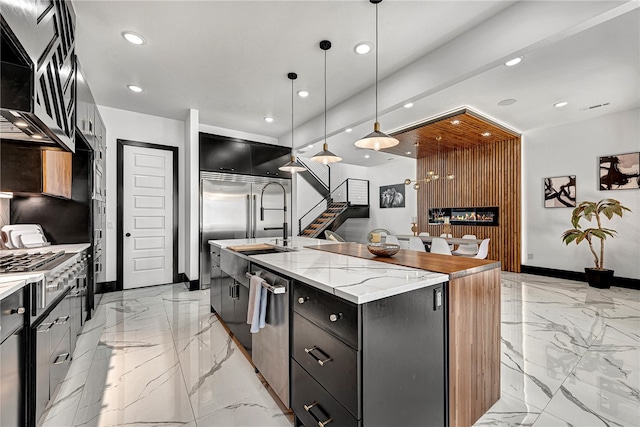 kitchen with stainless steel appliances, hanging light fixtures, a center island with sink, and light stone counters