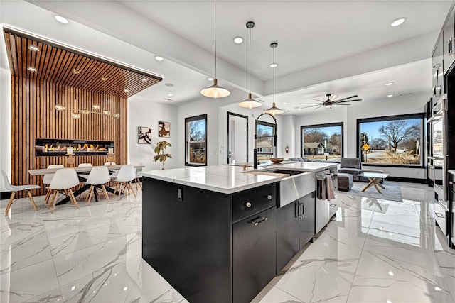 kitchen featuring an island with sink, ceiling fan, sink, pendant lighting, and a fireplace