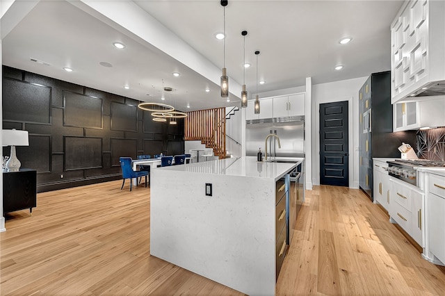 kitchen with a large island with sink, pendant lighting, white cabinetry, light hardwood / wood-style flooring, and appliances with stainless steel finishes