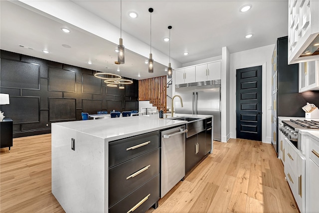 kitchen with pendant lighting, white cabinets, a center island with sink, light hardwood / wood-style flooring, and stainless steel appliances