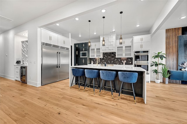 kitchen with pendant lighting, built in appliances, light hardwood / wood-style floors, and backsplash