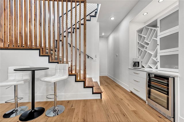 stairs with beverage cooler, hardwood / wood-style floors, and bar area