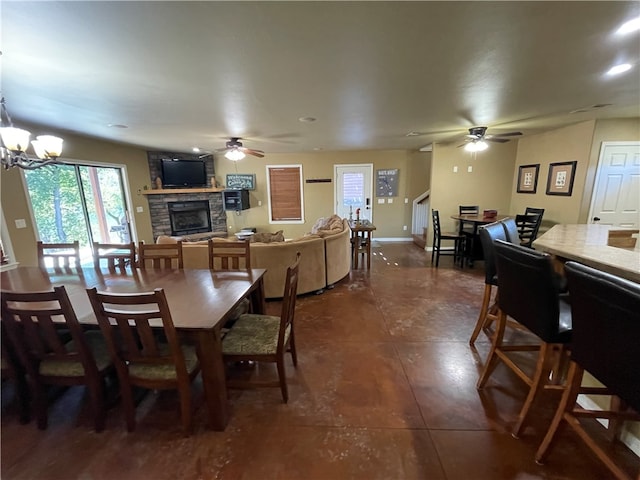 dining room with a fireplace, ceiling fan with notable chandelier, and dark tile patterned flooring