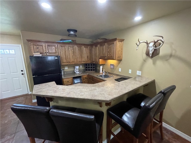 kitchen featuring black refrigerator, sink, kitchen peninsula, tile patterned floors, and a kitchen breakfast bar