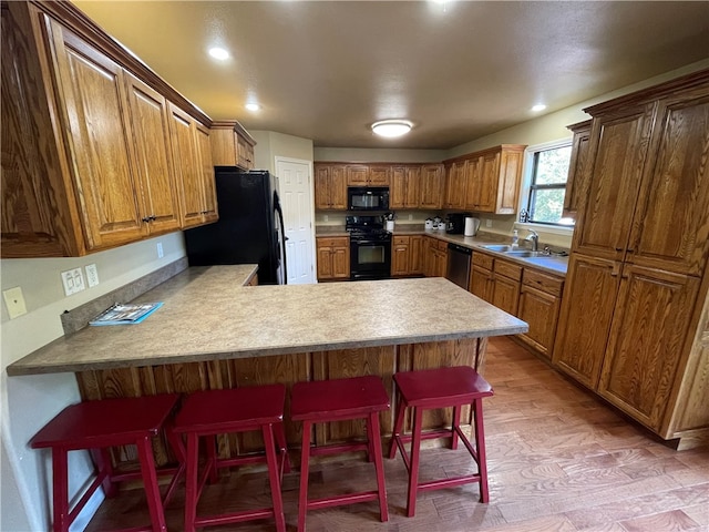 kitchen featuring light hardwood / wood-style floors, a breakfast bar area, sink, kitchen peninsula, and black appliances