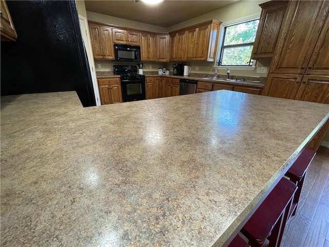 kitchen featuring kitchen peninsula, dark hardwood / wood-style floors, a breakfast bar area, and black appliances