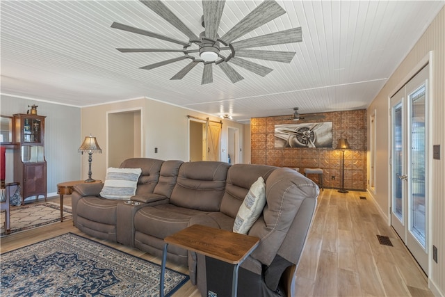 living room featuring ceiling fan, light wood-type flooring, crown molding, and a barn door