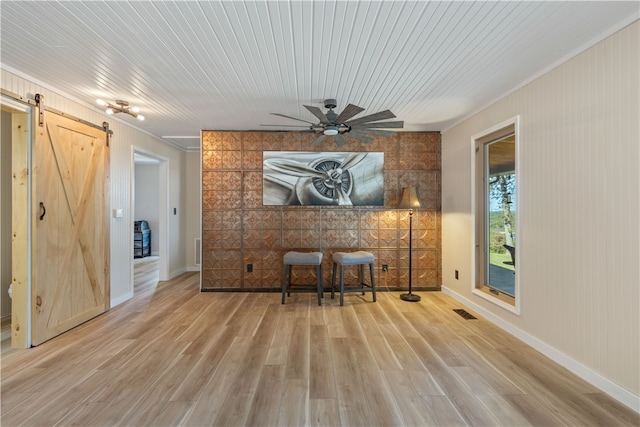 unfurnished room with a barn door, crown molding, light hardwood / wood-style flooring, and ceiling fan