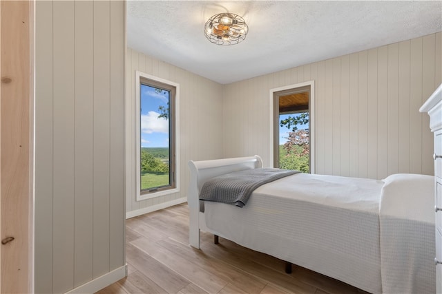 bedroom featuring a textured ceiling, wood walls, light hardwood / wood-style floors, and multiple windows