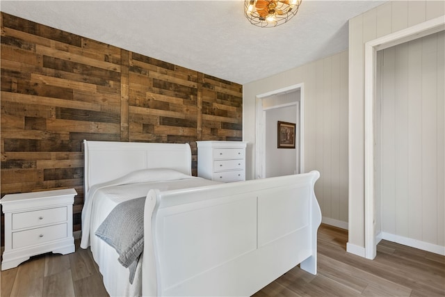 bedroom featuring hardwood / wood-style flooring, wood walls, and a textured ceiling