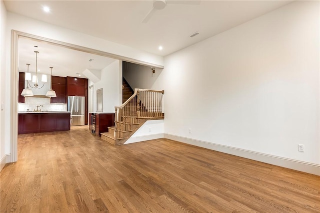 unfurnished living room featuring ceiling fan with notable chandelier, sink, and light wood-type flooring