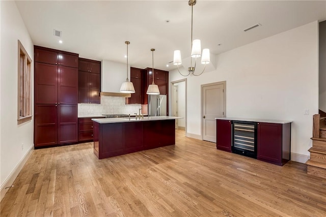 kitchen with pendant lighting, beverage cooler, an island with sink, backsplash, and stainless steel fridge