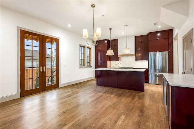 kitchen featuring wood-type flooring, stainless steel refrigerator, hanging light fixtures, french doors, and backsplash