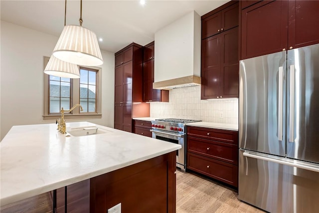 kitchen featuring appliances with stainless steel finishes, decorative light fixtures, light hardwood / wood-style floors, sink, and custom range hood